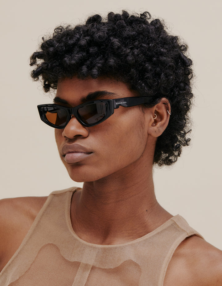 A modern cat-eye silhouette featuring frame beveling, bespoke wavy temple shape and "ribbed" inner tip grips. -Handcrafted from bio-circular acetate -Poly Renew lenses made with 50% recycled plastic -Five barrel hinges with coated safety screws Complete with lens cloth and collapsible pyramid case. 