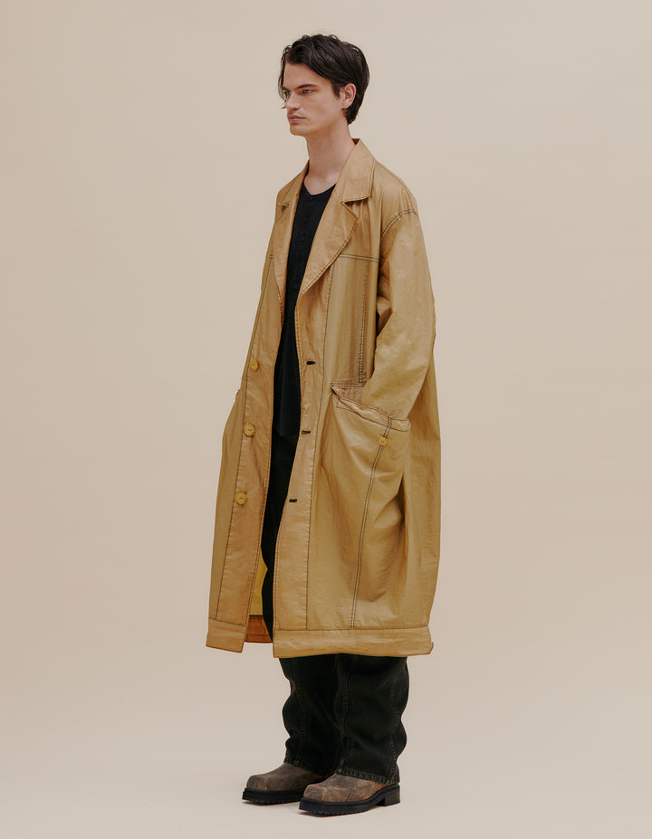 Oversized trench coat with button front. Made from an Italian coated nylon featuring a subtle sheen. Unlined, with felled seams throughout. Garment wash with black topstitching and exaggerated pocket details. Model wears size M. 60% nylon, 40% polyurethane. Made in USA.