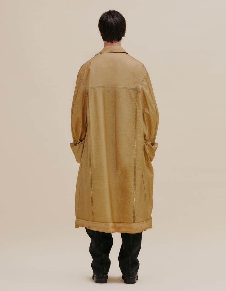 Oversized trench coat with button front. Made from an Italian coated nylon featuring a subtle sheen. Unlined, with felled seams throughout. Garment wash with black topstitching and exaggerated pocket details. Model wears size M. 60% nylon, 40% polyurethane. Made in USA.