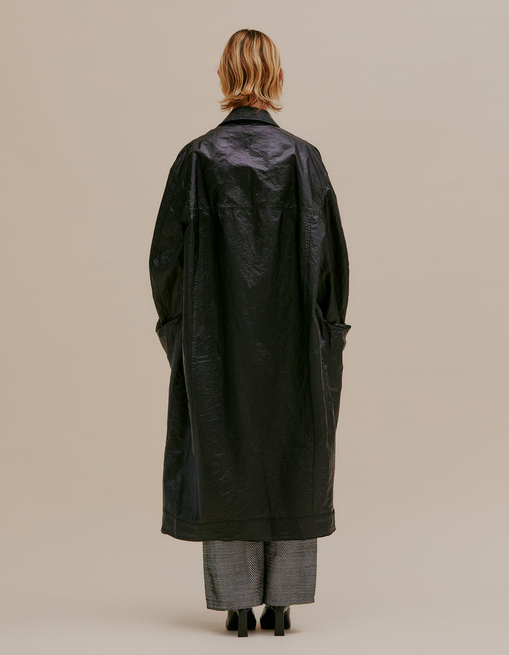 Oversized trench coat with button front. Made from an Italian coated nylon featuring a high sheen. Unlined, with felled seams throughout. Garment wash with black topstitching and exaggerated pocket details. Model wears size M. 60% nylon, 40% polyurethane. Made in USA.
