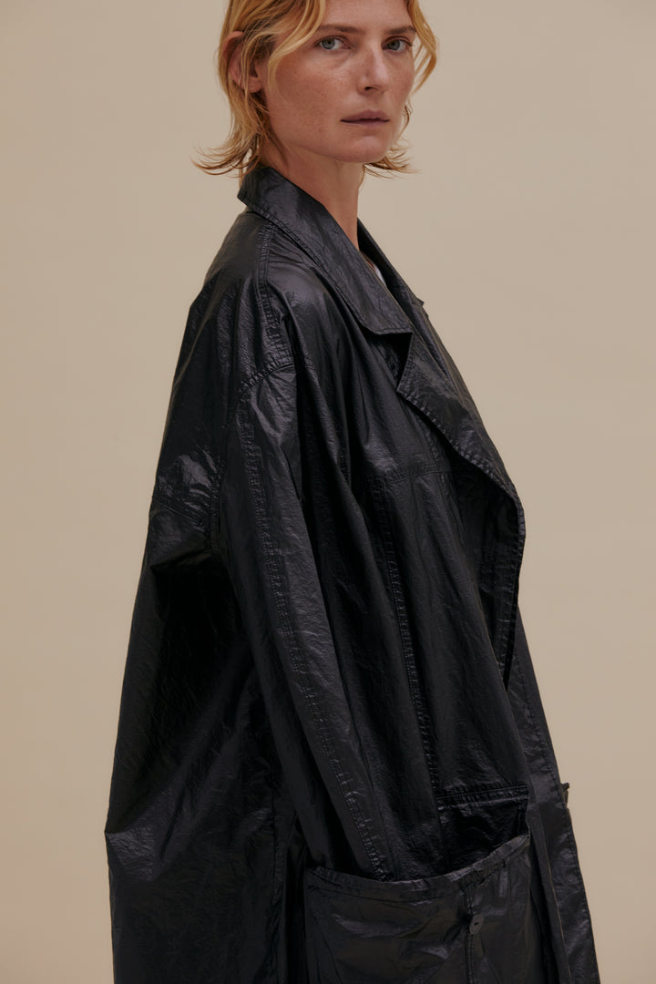 Oversized trench coat with button front. Made from an Italian coated nylon featuring a high sheen. Unlined, with felled seams throughout. Garment wash with black topstitching and exaggerated pocket details. Model wears size M. 60% nylon, 40% polyurethane. Made in USA.